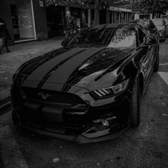 a black and white photo of a mustang parked on the side of the road in front of a building