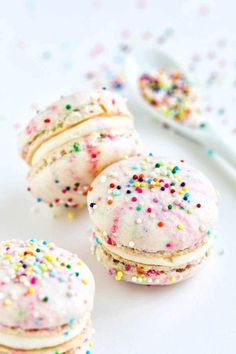 three white cookies with sprinkles and a spoon on the table next to them