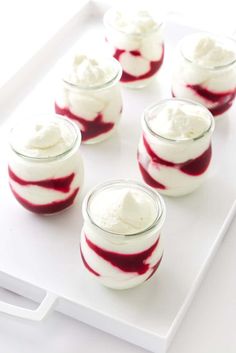 four desserts with red and white toppings in small glass bowls on a tray