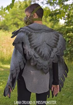 a woman wearing a bird costume in the grass with her back turned to the camera