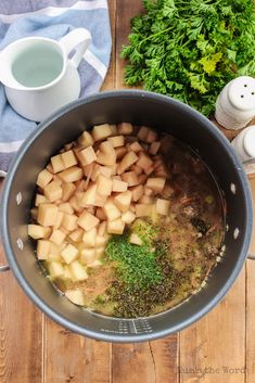 potatoes and herbs in a pot on a wooden table next to a cup of tea