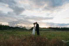 a bride and groom standing in a field at sunset