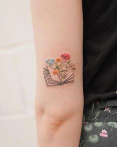 a woman with a tattoo on her arm holding an open book and flowers in it