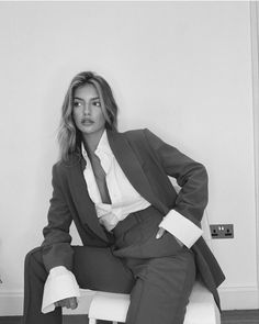 a woman sitting on top of a white chair wearing a suit and tie with her hands in her pockets