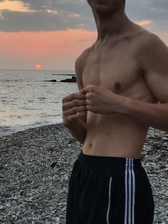 a man standing on top of a rocky beach next to the ocean at sun set