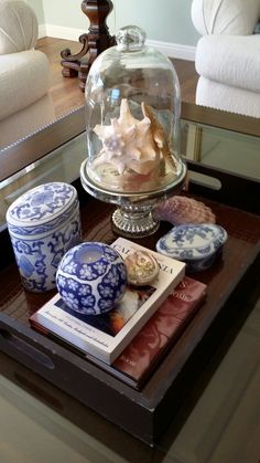 a coffee table topped with blue and white dishes next to a glass clochet