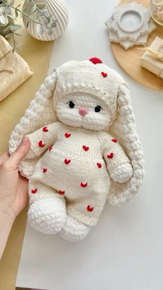 a hand holding a white knitted stuffed animal with red hearts on it's body