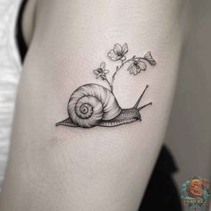 a small snail tattoo on the back of a woman's leg, with flowers growing out