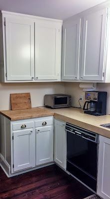 an empty kitchen with white cabinets and wood flooring on the counter top, along with black appliances