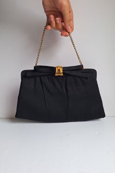 A black and gold evening bag with a gorgeous gold and black diamante encrusted lift up clasp featuring a black fabric bow. The bag also has a gold tone chain top handle, which can hide away inside, so it can be used as a top handle bag or a clutch bag.  Inside there is a black satin lining and one main compartment, if you look carefully you can see a logo on the lining by the brand After Five. There is also a black coin purse attached to the bag by an elasticated string.   Dimensions: Height: 14 Gold Evening Bag, Satin Noir, Fifties Fashion, Chain Top, Bag Inside, Un Logo, Fabric Bows, Bag Vintage, Clutch Handbag