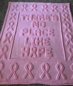 a pink crocheted blanket with words and ribbons on it