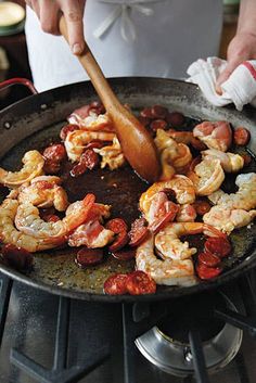 a person cooking shrimp and sausage in a skillet on the stove with a wooden spatula