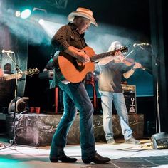 two men are playing guitars on stage at a concert, one is wearing a cowboy hat and the other has a guitar