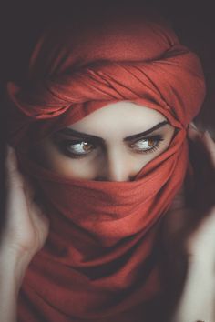 a woman with blue eyes wearing a red scarf over her head and covering her face