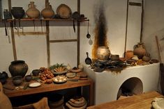 an old fashioned kitchen with pots and pans on the stove, wood table and shelves