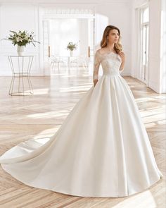 a woman in a white wedding dress standing on a wooden floor with her hands behind her back