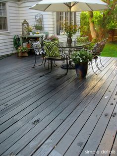 an outdoor patio with tables and umbrellas on it's decking area in front of a white house