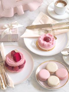 pink and white desserts on plates next to silverware, utensils and a cup of coffee