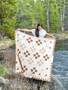 a woman is holding up a quilt by the water