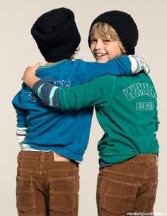 two young boys hugging each other while wearing beanies