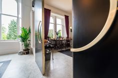 an open door leading to a dining room with large windows and potted plants in the corner