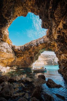 a boat is in the water near an arch shaped rock formation that looks like it's coming out of the ocean