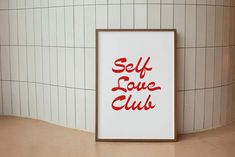 there is a sign that says self love club next to a wall with white tiles