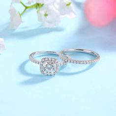 two wedding rings with diamonds on top and flowers in the background next to each other