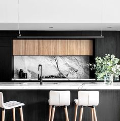 three stools sit in front of an island with marble counter tops and black cabinets