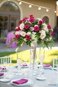 a tall vase filled with pink and white flowers on top of a table covered in plates