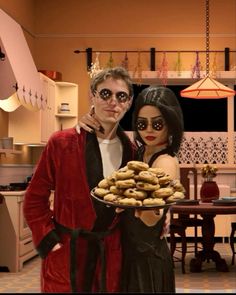 a man and woman dressed in costumes holding a tray of doughnuts with an image of a skeleton behind them