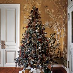 a christmas tree with presents under it in a living room next to a wall painting