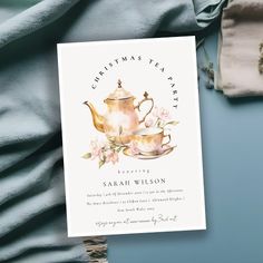 a christmas tea party card with a teapot and flowers on it next to some blankets