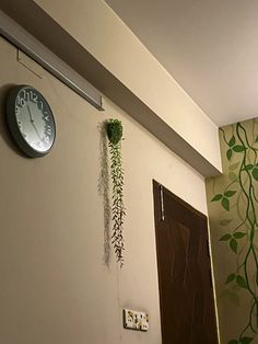 a clock mounted to the side of a wall next to a plant hanging from it's side