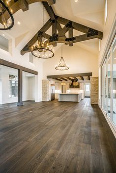 an empty room with wooden floors and chandeliers hanging from the ceiling, in front of large windows