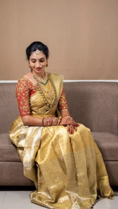 a woman sitting on top of a couch wearing a yellow dress and gold sari