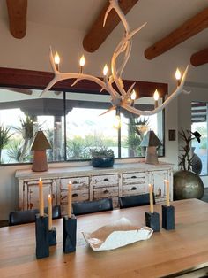 a dining room table with candles on it and an antler head hanging from the ceiling