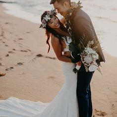 a bride and groom standing on the beach with their arms around each other as they kiss