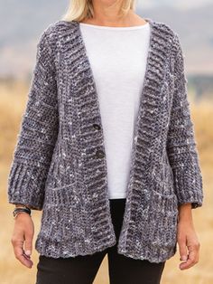 a woman standing in a field wearing a gray cardigan