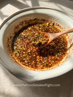 a wooden spoon in a white bowl filled with chili and seasoning on top of a table