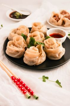 some dumplings are sitting on a plate with chopsticks next to them and sauce