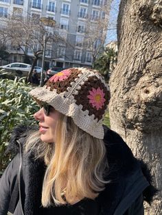 a woman standing next to a tree wearing a crocheted hat with flowers on it