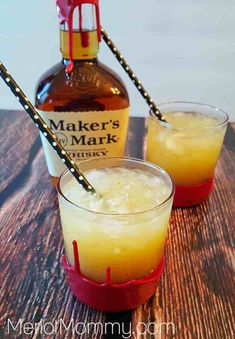 two glasses filled with liquid sitting on top of a wooden table next to a bottle