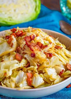 a white bowl filled with cabbage and bacon on top of a blue cloth next to a knife