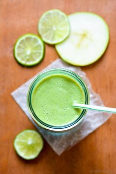 a glass filled with green smoothie next to sliced limes