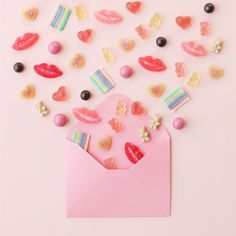 an envelope filled with candy and candies on top of a pink surface next to a pile of hearts