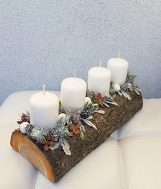 candles are placed on a log with greenery and pine cones