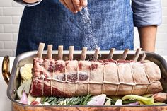 a person sprinkling seasoning onto a rack of meat in a roaster