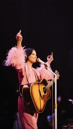 a woman holding a guitar while standing in front of a microphone