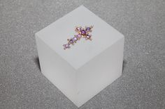 a diamond cross brooch sits on top of a white box